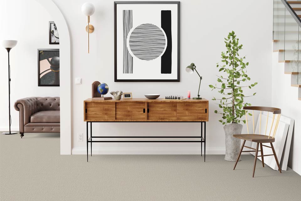 grey carpet in entryway with entryway table and chair with wall art.